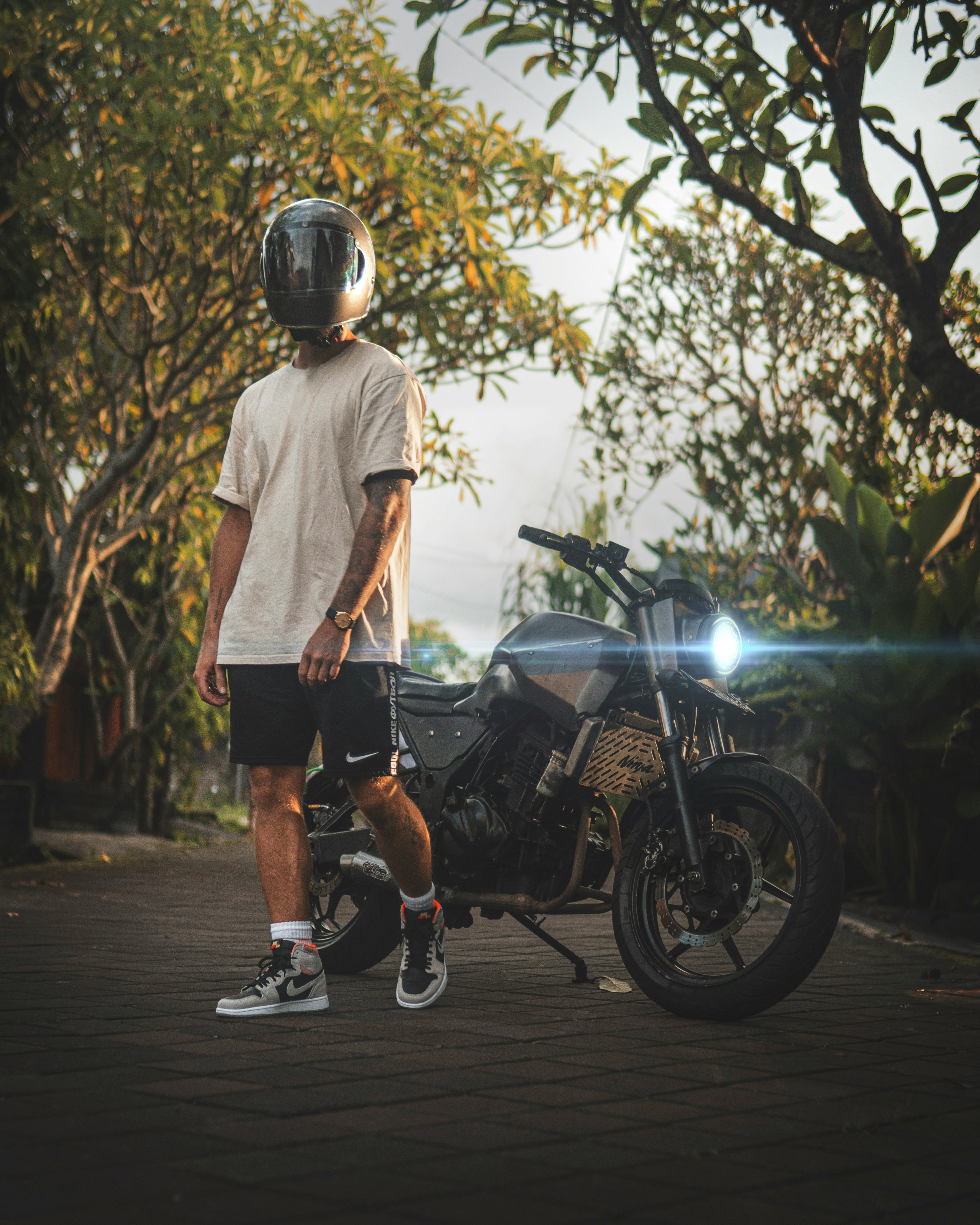 man in white crew neck t-shirt and black shorts standing beside black motorcycle during daytime